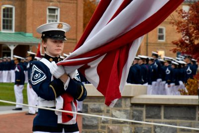 A female cadet in dress uniform grasps the flag as part of a ceremony on Veterans Day.