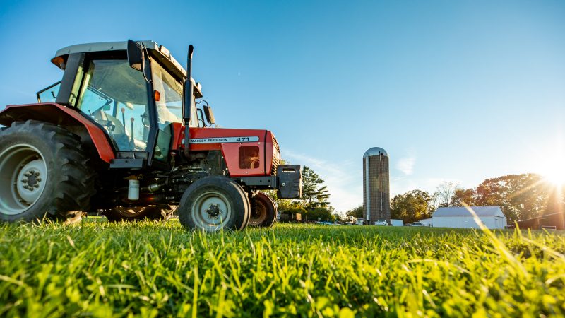 A tractor sitting in a grassy field with a silo in the background