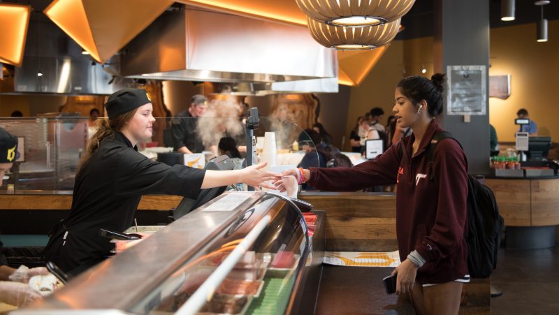 A staff member hands a student their card at the cash register