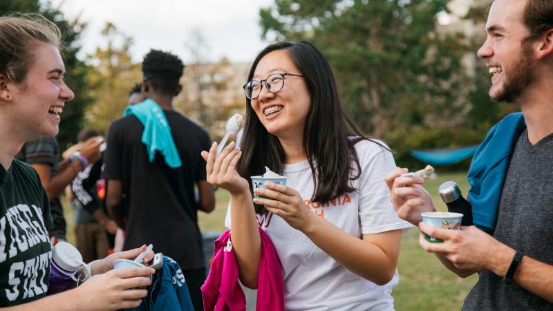 A group of students standing in an outdoor space, laughing and eating ice cream