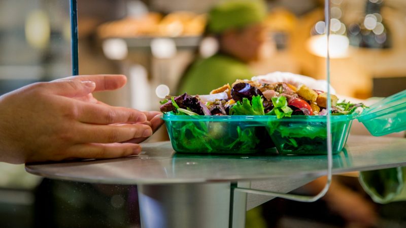 Reusable to-go container being handed form one person to another