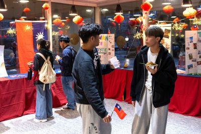 In a colorfully decorated room, two students in the foreground talk with each other while students in the background view displays on tables.