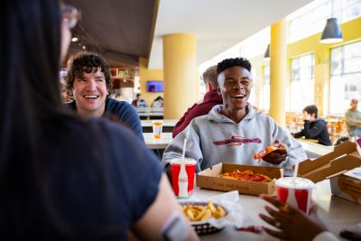 Two people smiling enjoying pizza in dining hall